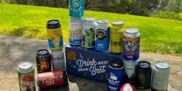 Cans of beer surrounding a WABA Drink West Drink mixed pack